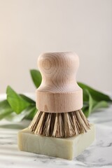 One cleaning brush and bar of soap on white marble table, closeup