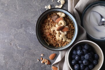 Tasty granola in bowl, blueberries and yogurt on gray textured table, flat lay. Space for text