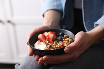 Obraz na płótnie Canvas Woman holding bowl of tasty granola with berries, yogurt and seeds indoors, closeup