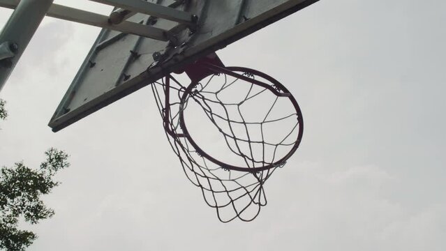 View from below of ball being thrown in basketball ring with net on cloudy day outdoorsView from below of ball being thrown in basketball ring with net on cloudy day outdoors
