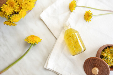 Bottle of dandelion tincture or oil, flower bunch and vitamins on a white marble table. Herbal...