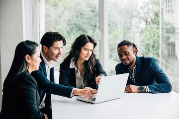 In an office meeting room both men and women in diverse business team work together on laptop. Their teamwork, collaboration and togetherness are apparent they discuss, plan and strategize for success