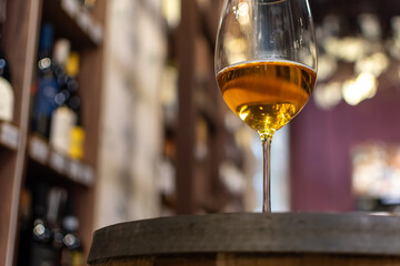 Glass with wine on oak barrel close-up on blurred background of wine shelves