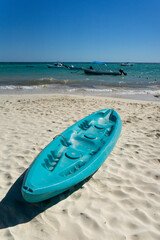 Tropical beach in Mexico with turquoise kayaks on white sand, blue sky and calm sea with boats in...