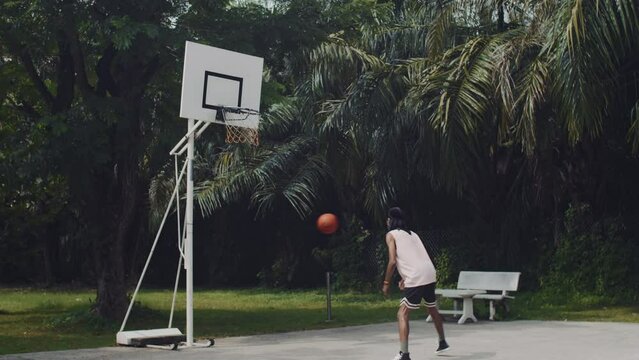 Wide shot of black male streetball player throwing ball in ring while training on outdoor playground