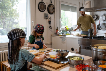 Father cooking and his two daughters dressed in their aprons and hats preparing sushi in the kitchen, rolling up and laying out the rice with vegetarian makis. Family in the kitchen learning