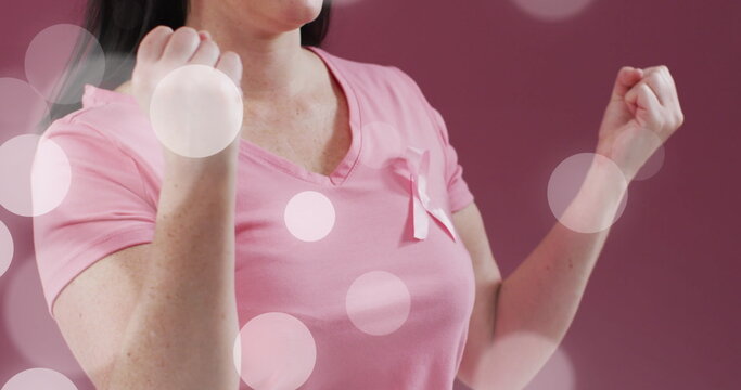 Image of light spots over caucasian woman with pink ribbon on pink background