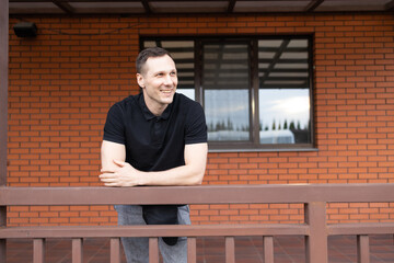 Portrait of a happy middle-aged man in a black T-shirt standing in front of house.
