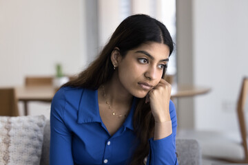 Frustrated unhappy young Indian woman thinking on bad news, problems, troubles, leaning face on hand, looking away with apathy, melancholy, boredom, feeling burnout, emotional crisis, depression