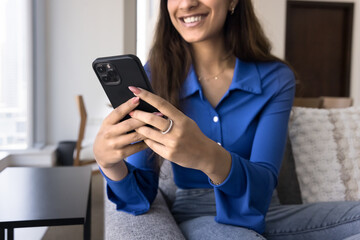 Close up of mobile phone in hands of happy young 20s girl typing message, smiling, laughing, chatting online, browsing Internet content, enjoying wireless technology. Cropped shot