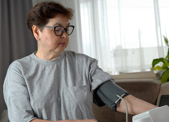Senior woman with hypertension measuring blood pressure herself at home, close-up.