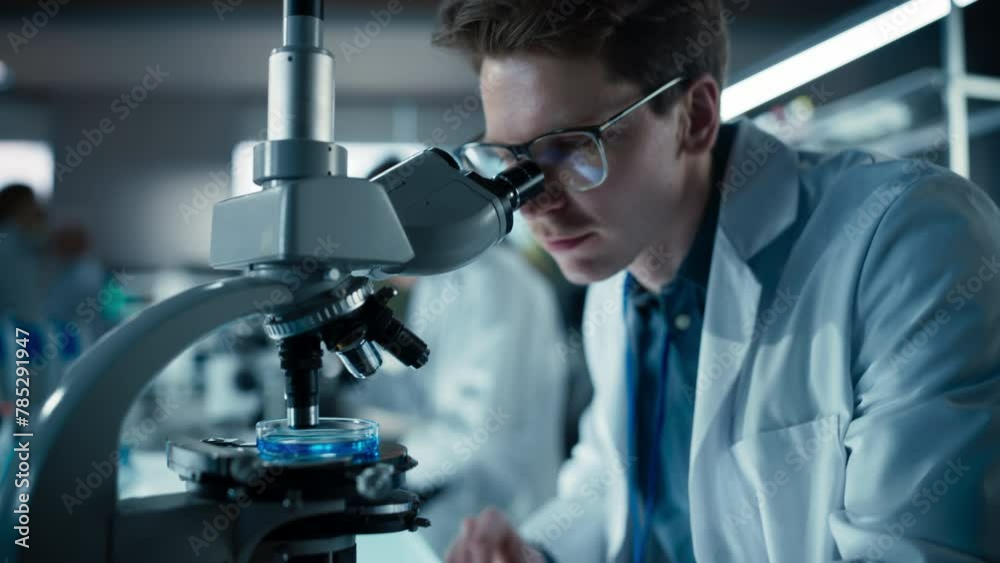 Poster close up portrait of a young microbiologist wearing glasses and looking through the microscope, anal