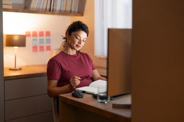 A focused pregnant woman taking notes in her notebook while working from home