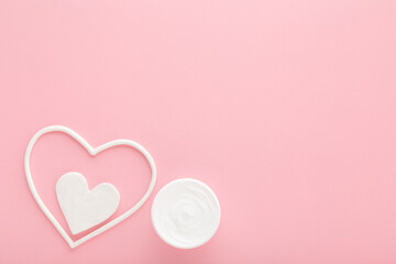White heart shapes with cream jar on light pink table background. Pastel color. Care about female face, hands, legs and body skin. Closeup. Empty place for text. Top down view. - 785292719