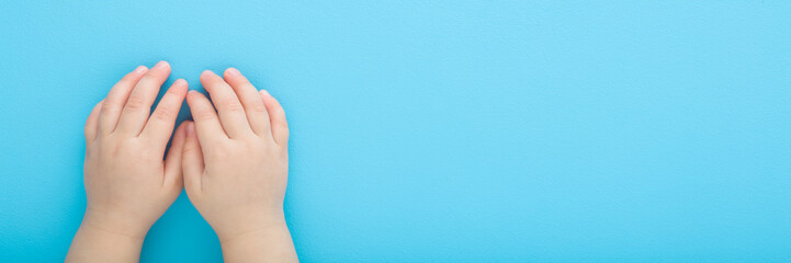 Baby boy hands on light blue table background. Pastel color. Closeup. Point of view shot. Empty place for text. Wide banner. Top down view.