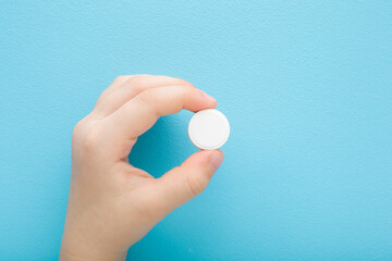 Baby hand holding white pill of c vitamin on light blue table background. Pastel color. Receiving nutrition supplement. Closeup. Top down view. - 785292741