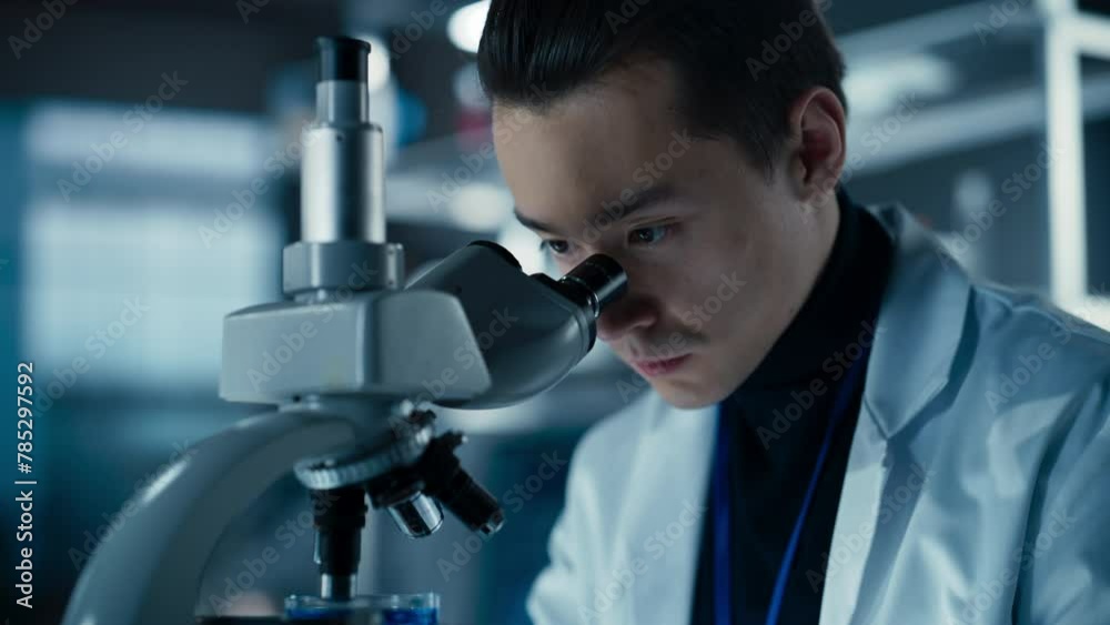 Poster Portrait of a Handsome Chemistry Student Working on a Research Project in University. Medical Research Scientist Looking at Biological Samples Under a Microscope in an Applied Science Laboratory