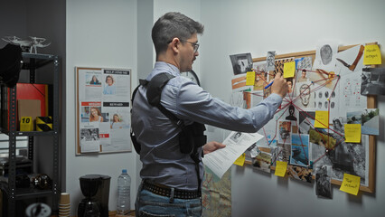 Hispanic man analyzing a crime investigation board with photos and notes in a detective's office