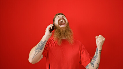Overjoyed young redhead man ecstatically celebrating while speaking on the phone over an isolated...