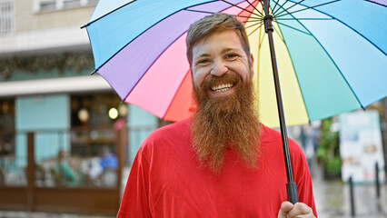 Young redhead man smiling confident holding umbrella at street
