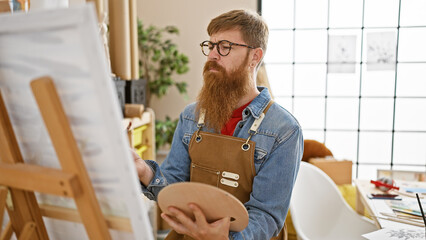 Handsome redhead guy, a young artist engrossed in drawing at his art studio, rocking a beard, apron...