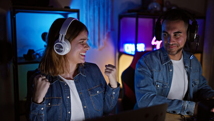 A joyful man and woman wearing headphones in a gaming room with neon lights compete in a video game...