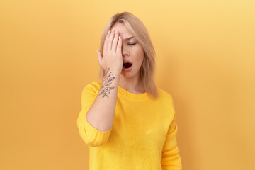 Young caucasian woman wearing yellow sweater yawning tired covering half face, eye and mouth with...