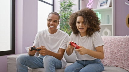 Joy-filled beautiful couple enjoy playing video game on their comfortable sofa, exuding confidence...