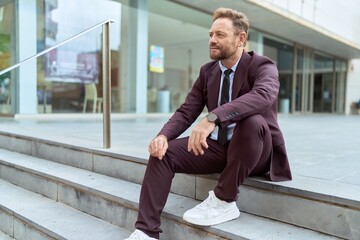 Middle age man business worker sitting on stairs with relaxed expression at street
