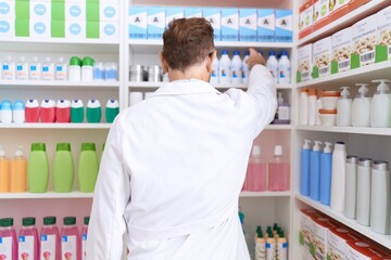Middle age man pharmacist holding product on shelving at pharmacy