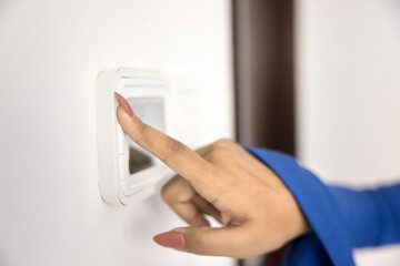 Young woman using climate control panel at home, regulating thermostat, air temperature in apartment, pressing button on wall mounted device with display. Close up of hand and smart home gadget