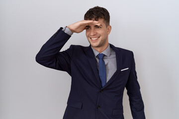 Young hispanic business man wearing suit and tie very happy and smiling looking far away with hand over head. searching concept.