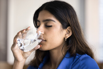 Beautiful young 20s Indian girl with closed eyes enjoying fresh pure water, drinking cold beverage...