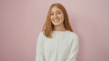 A smiling young caucasian woman with red hair dressed in a white sweater isolated against a pink...