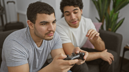 Two young hispanic men focusing intently on playing a video game together in a cozy indoor setting.