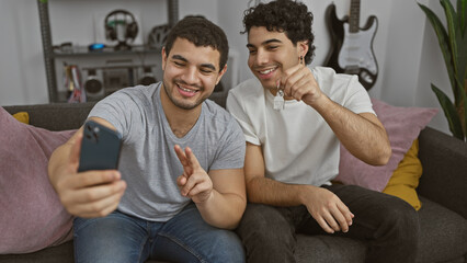 Two men take a selfie on a couch with a house key, symbolizing friendship and new beginnings...