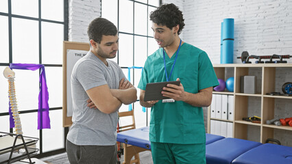 A male physiotherapist with a tablet discusses treatment with a patient in a modern rehab clinic.