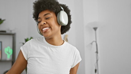 Smiling african american woman enjoys music on headphones in a cozy living room.