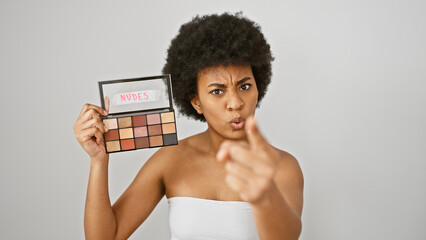 A displeased black woman holds a palette of nude eyeshadows, pointing while on a white background.