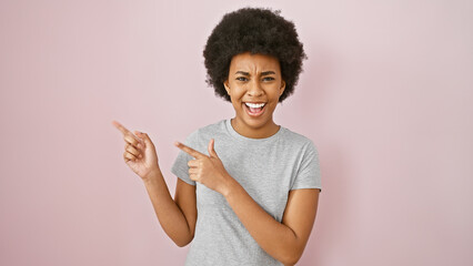 Portrait of a cheerful african american woman with curly hair pointing aside on a pink background.