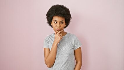 Thoughtful african american woman with curly hair posing against a pink wall, exuding confidence...