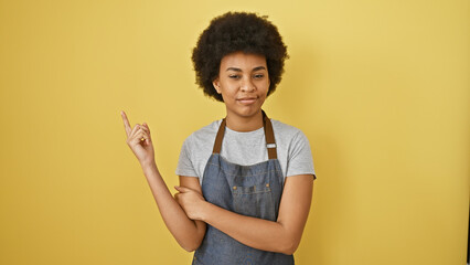 Confident african american woman with curly hair posing in casual clothes against a vibrant yellow...