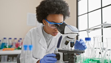 African american female scientist analyzing samples with a microscope in a laboratory setting.