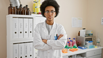 Confident african american female scientist standing with arms crossed in a laboratory setting,...