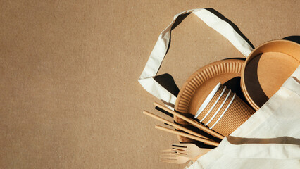 A set of paper utensils and wooden cutlery in fabric bag on a brown background. Eco friendly, zero...