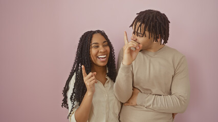 A joyful couple on a pink background with the woman gesturing an idea as the man looks on with...