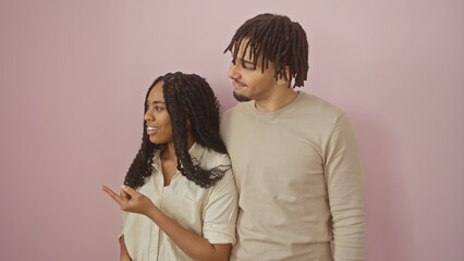 A man and woman stand side by side against a pink wall, looking away with a sense of togetherness.