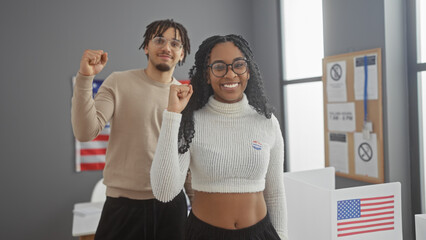 A cheerful man and woman with 'i voted' stickers, raising their fists in unity at an american polling station, symbolizing democratic participation.