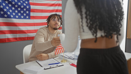 A man hands a voting sticker to a woman in a room with an american flag, symbolizing electoral...