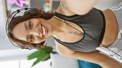 Young woman with headphones smiling indoors, tattoos visible, suggesting a music or radio studio...